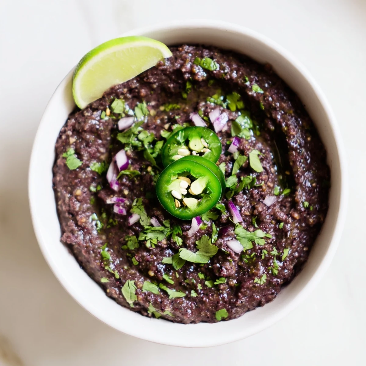 Creamy Spicy Black Bean Dip, garnished with fresh cilantro and a wedge of juicy lime.