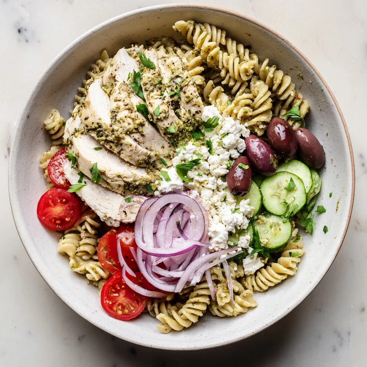 Juicy lemon-herb chicken slices rest atop a colorful Greek Chicken Pasta Bowl with olives, tomatoes, and creamy feta.