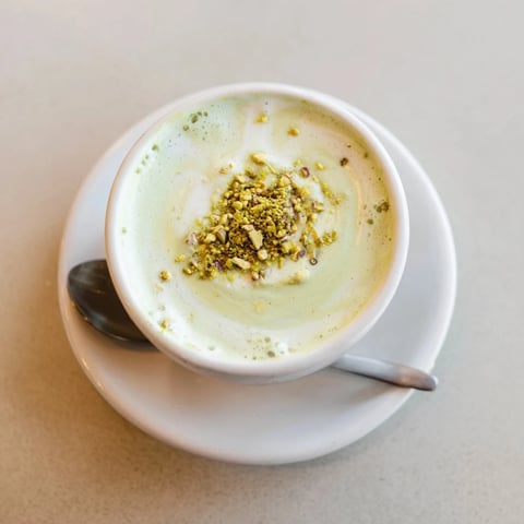 Creamy pistachio milk latte topped with froth and crushed nuts for flavor.  