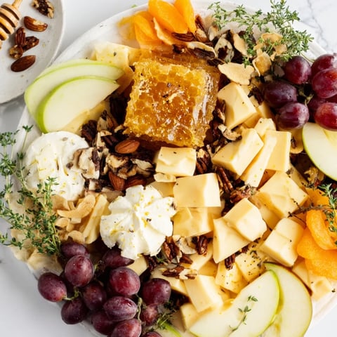 Honeycomb-shaped Busy Bee Snack Plate overflows with cheese, fruit, and honey, perfect for sharing.