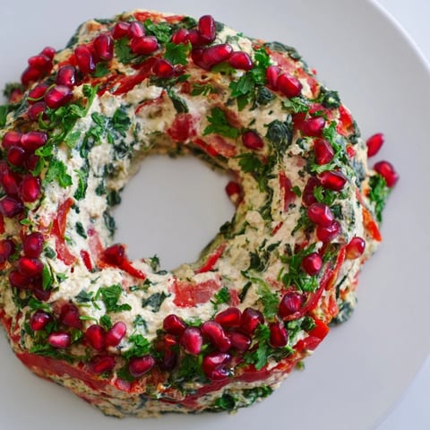 Festive red pepper and spinach dip wreath garnished with vibrant parsley and pomegranate seeds, perfect for entertaining.