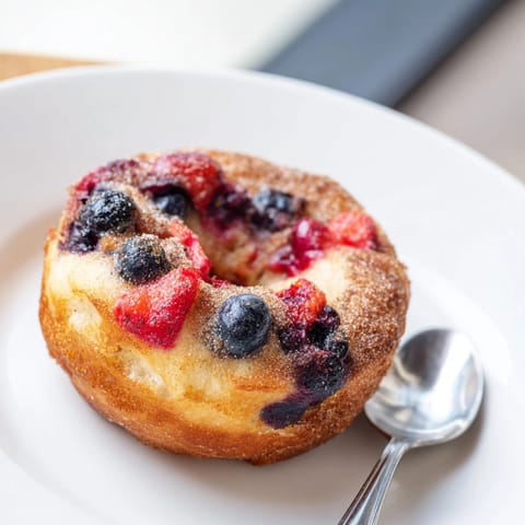 Warm, baked Protein Cinnamon Berry Doughnuts, bursting with berries, await a cinnamon sugar dusting.