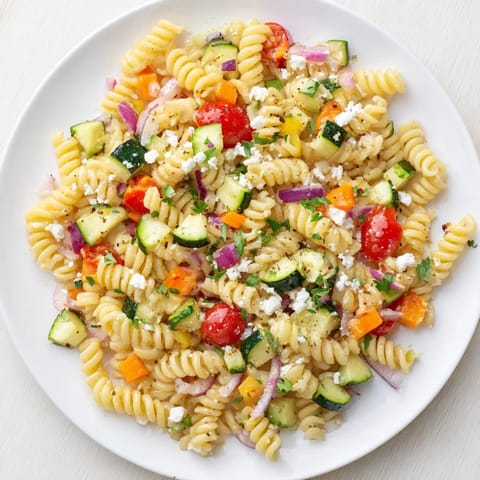 Freshly assembled pasta salad with bright seasonal vegetables and crumbled feta cheese visible.