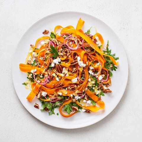 A close-up of Roasted Carrot Ribbon Salad showing crumbled feta and toasted pecans on fresh arugula and spinach.  