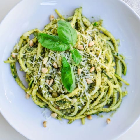 Zucchini noodles with pesto sautéed until tender-crisp, garnished with fresh basil and pine nuts, served warm as a vibrant Italian-inspired main dish.