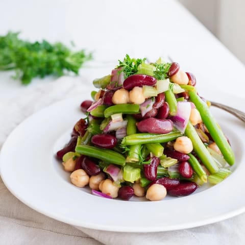 Close-up of chilled Three-Bean Salad garnished with fresh parsley, showcasing colorful beans and crisp celery slices.