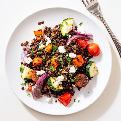 Hearty Black Lentil Salad with Roasted Vegetables is served warm, tossed with fresh parsley and crumbled feta on a rustic platter.