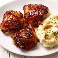 Golden, glistening honey BBQ chicken thighs served beside fluffy garlic mashed potatoes, a complete dinner.